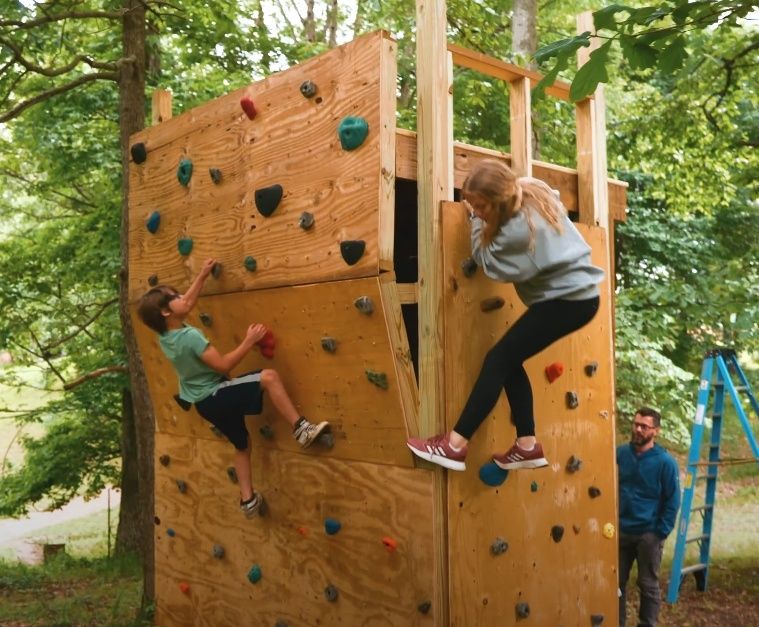 Två barn klättrar på en hög klätterställning i skogen